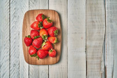 Beyaz bir masada tahta bir tahtanın üzerinde kırmızı çileklerin üst görüntüsü..