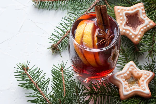 Mulled wine in glass mug with a lemon, cinnamon sticks, home-made cookies and star anise on white table