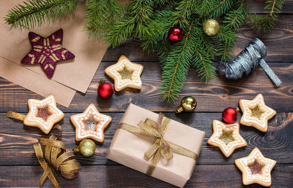 Різдвяний подарунок на дерев'яному коричневому столі з ялиновими гілками, домашнім печивом та ялинковими іграшками . — стокове фото