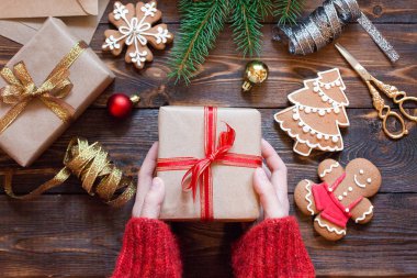 Kadınların elleri, içinde ladin dalları, zencefilli ekmek ve Noel ağacı oyuncakları olan ahşap bir masanın üzerinde bir hediye tutuyor.. 