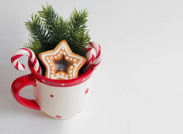 Copo de Natal com pirulitos, ramos de abeto e biscoitos caseiros na forma de uma estrela na superfície branca . — Fotografia de Stock