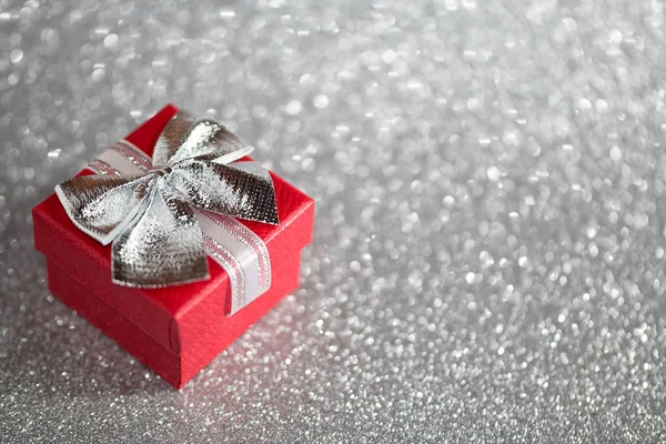 Red gift box with silver bow on silver glitter surface with bokeh lights. — Stock Photo, Image