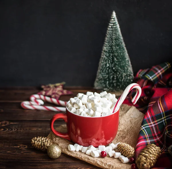 Kırmızı fincanlar ve çizgili çubuk şekerlemelerle kapuçino, ahşap masada köknar konileri.. 