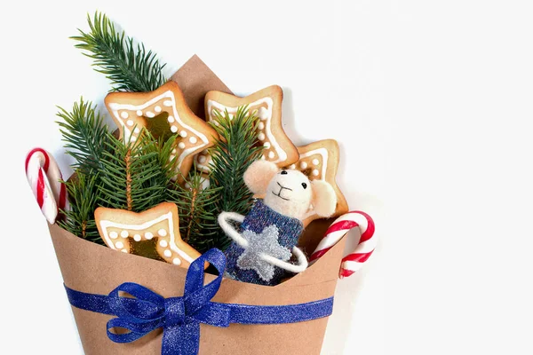 Presente de Natal em um saco de papel com um mouse branco de brinquedo, pirulitos, biscoitos caseiros e ramos de abeto em um fundo branco . — Fotografia de Stock