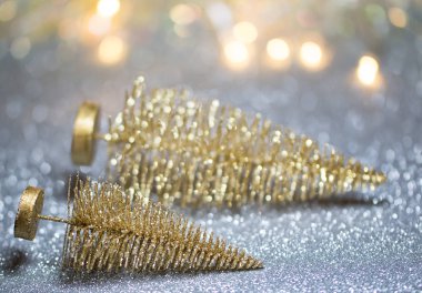 İki küçük Altın Noel ağacı gümüş bir yüzeye uzanır. Arka planda bokeh ışıkları vardır.. 