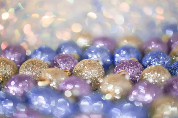 Imagen borrosa de brillantes juguetes de Navidad violetas, azules y dorados sobre fondo brillante. Foco suave y hermoso bokeh . —  Fotos de Stock