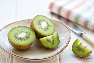 Bıçak ve çizgili keten peçeteyle birlikte açık ahşap bir masada taze kivi meyvesi dilimlenmiş. Ön görünüm.