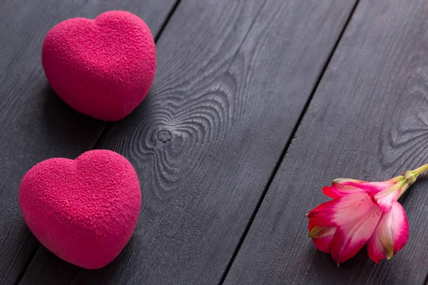 Concepto de San Valentín. Dos pastel de terciopelo corazón rosa sobre un fondo negro de madera con una delicada flor de Alstroemeria — Foto de Stock