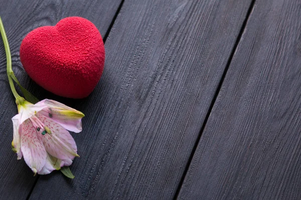 Concepto de San Valentín. Pastel de terciopelo corazón rojo sobre fondo negro de madera con una delicada flor de Alstroemeria — Foto de Stock