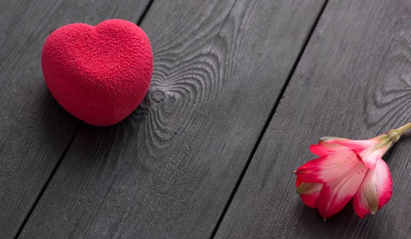 Concepto de San Valentín. Pastel de terciopelo corazón rojo sobre fondo negro de madera con una delicada flor de Alstroemeria — Foto de Stock