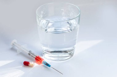 Bir kapsül hapı, aşılı şırınga ve gri arka planda bir bardak su...