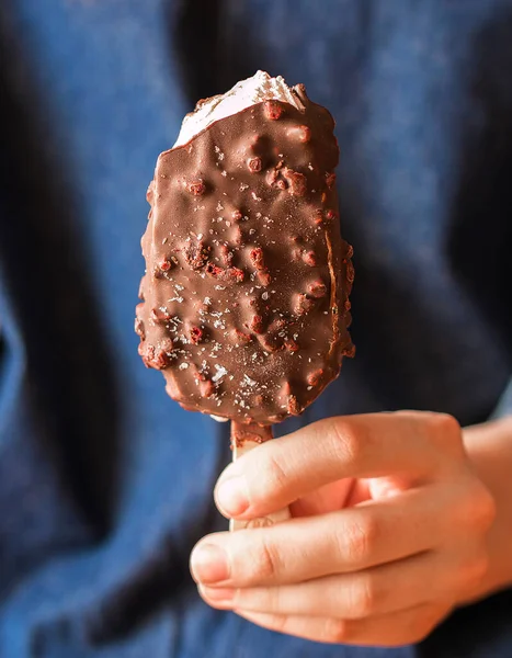 Čokoládová zmrzlina s čokoládou a jahodovým povlakem v dámské ruce.Detailně. Dívka v modrých šatech drží čokoládovou zmrzlinu — Stock fotografie