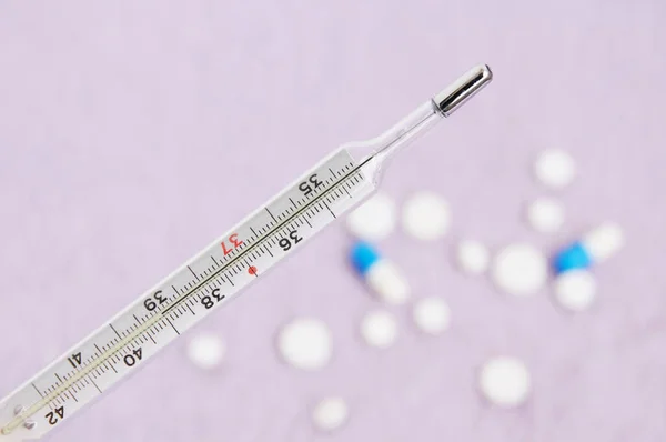 Mercury thermometer and heap of medical tablets isolated on a white background
