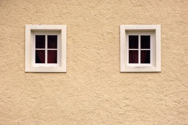 Eski moda bir Avrupa evinin sarı cephe duvarında iki pencere.