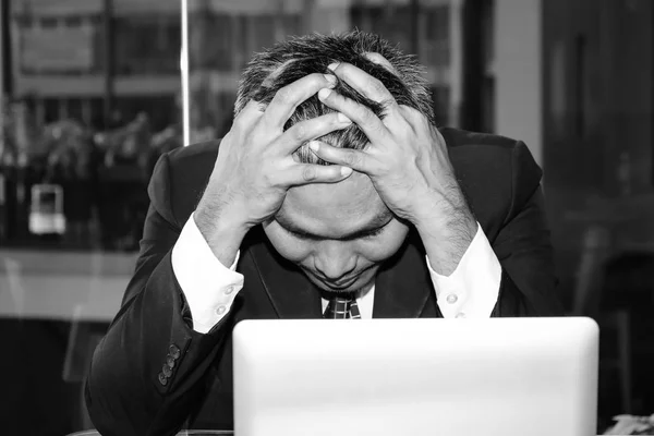 Un bărbat de afaceri asiatic este trist și plânge în fața laptopului computerului pentru managementul eșecului în activitatea de investigare a afacerilor financiare și locul de muncă în timpul unei probleme puternice de criză economică. Fotografie de stoc