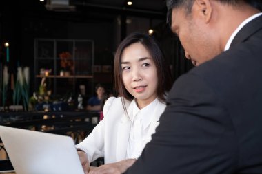 Resmi takım elbiseli Asyalı işadamı ve iş kadını, modern ofis yerinde yüksek teknoloji dizüstü bilgisayarlı çalışmaları tartışıyorlar.