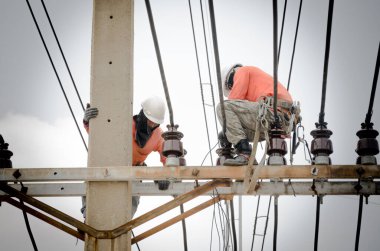 Teknisyenler elektrik direklerindeki yüksek voltaj iletim sistemlerini tamir ediyorlar..