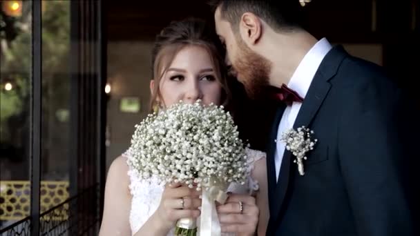 Жених шепчет слова любви невесте, прячась за букет — стоковое видео