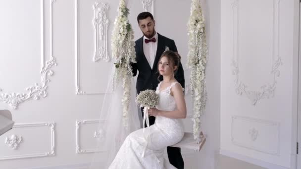 Наречений тримає плече нареченої в просторому залі з білими стінами — стокове відео