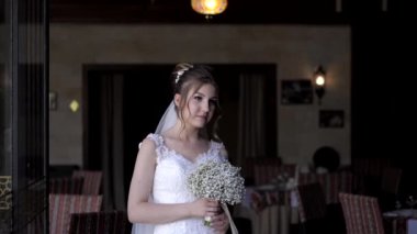 Gelin, restoranın içinde beyaz bir buket tutuyor.