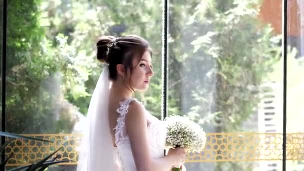 Noiva em vestido branco e véu poses perto de vidro câmera lenta — Vídeo de Stock