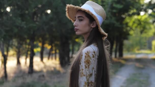 Senhora com cabelo escuro sob chapéu posa contra jardim embaçado — Vídeo de Stock