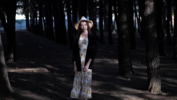 Νεαρή γυναίκα με κίτρινο ψάθινο καπέλο στέκεται στο σκοτεινό δάσος — Αρχείο Βίντεο