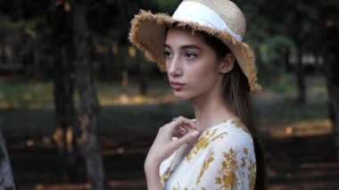 Kadın hasır şapkasını çıkarıp parkta poz veriyor.