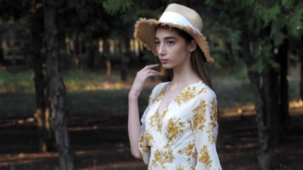 Donker harig meisje in stro hoed poseert tegen wazig park — Stockvideo