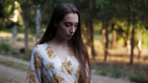 Mujer posa mirando a un lado contra el bosque borroso al atardecer — Vídeos de Stock
