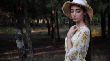 Beyaz elbiseli kadın ağır çekimde hasır şapkasını çıkarıyor.