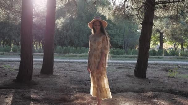 Długowłosy brunetka odkłada słomkowy kapelusz spacery wzdłuż parku — Wideo stockowe