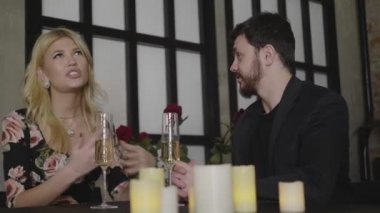 Uzun saçlı, renkli elbiseli, yorgun bir adamla konuşan bir sarışın.