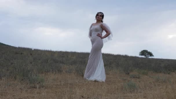 Dame in elegante witte jurk poses staande tussen leeg veld — Stockvideo
