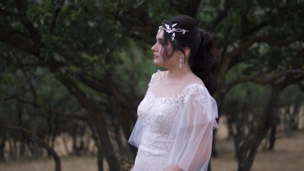 Novia posa mirando a la distancia contra las plantas verdes — Vídeo de stock