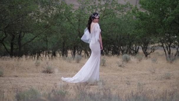 Beyaz elbiseli kadın yeşil ağaçlara karşı çayırda duruyor. — Stok video