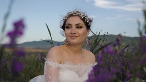Веселая невеста в кружевном платье в поле с фиолетовыми цветами — стоковое видео