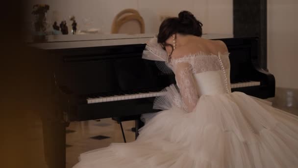 Novia en vestido con falda bouffant se apoya en el piano en la sala — Vídeos de Stock