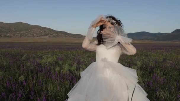 Ευτυχισμένη νύφη με υπέροχο φόρεμα ανάμεσα σε λουλούδια τη μέρα του ανέμου — Αρχείο Βίντεο
