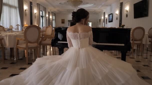 Bride in white dress with bouffant skirt plays piano in hall — 비디오