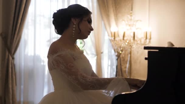 Грациозная невеста в белом платье со шнурками играет на пианино в зале — стоковое видео