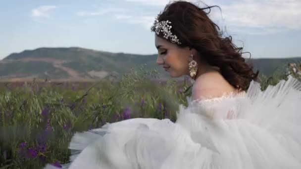Glad brud i snygg klänning luktar vilda blommor i fält — Stockvideo