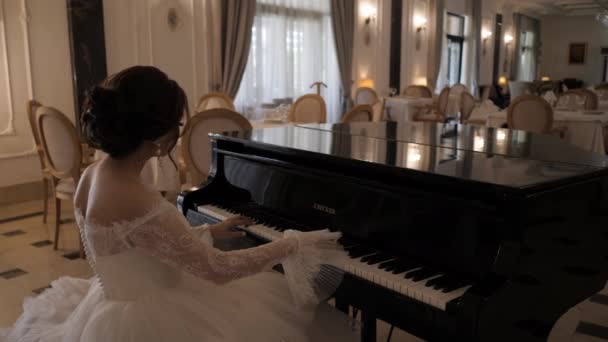 Elegante chica en vestido de novia toca el piano en el restaurante — Vídeos de Stock