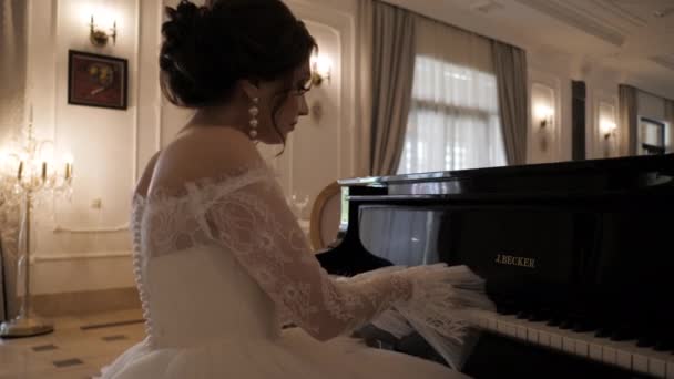Brunette bruid in mooie jurk speelt piano in bruiloft hal — Stockvideo