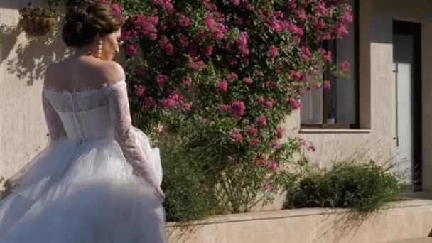 Glückliches Mädchen im eleganten Hochzeitskleid spaziert an Rosenbüschen vorbei — Stockvideo