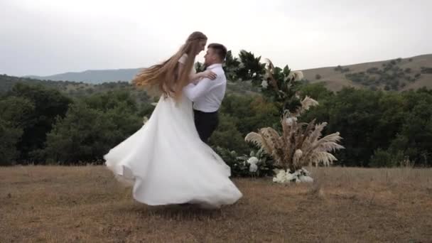 Novio musculoso remolinos sosteniendo novia de pelo largo en el prado — Vídeo de stock