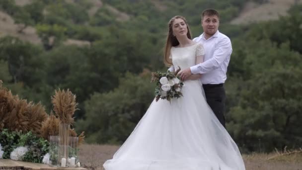 Dam i lång bröllopsklänning står i fiance kramar av plats — Stockvideo