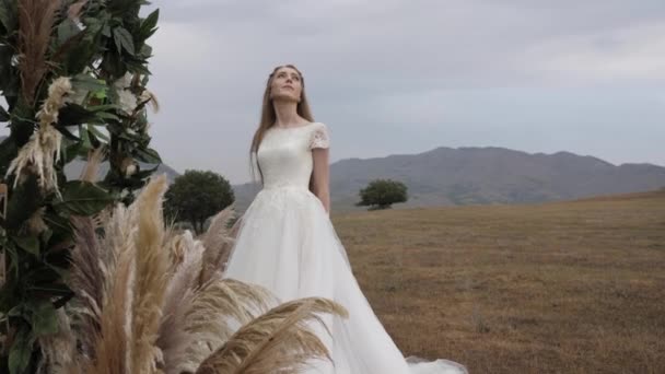 Брюнетка в длинном белом свадебном платье стоит возле украшений — стоковое видео