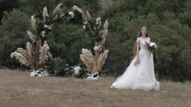 Junge Frau im langen weißen Hochzeitskleid steht auf Wiese — Stockvideo