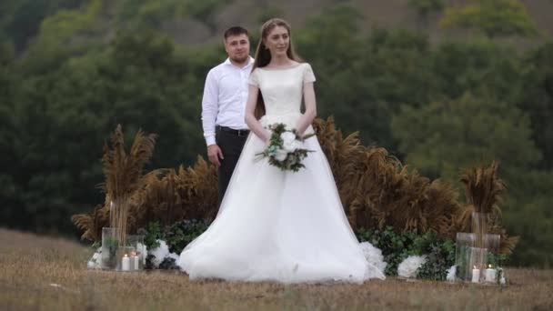 Beau fiancé se tient derrière la mariée en robe de mariée longue — Video